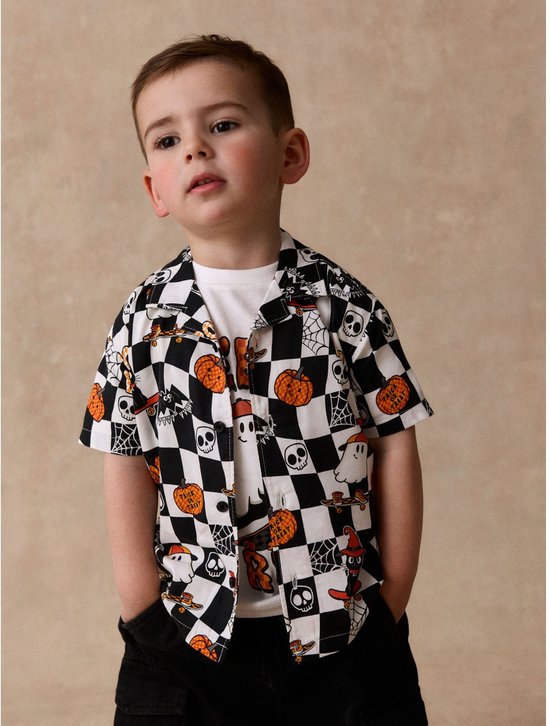 Jongen draagt een overhemd met Halloween-print, ruitjes, spoken en 'Trick or Treat'-tekst op een wit T-shirt.