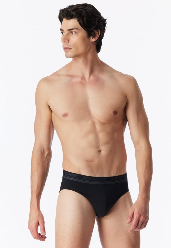 Man met zwarte slip met grijze band met UNCOVER-logo.