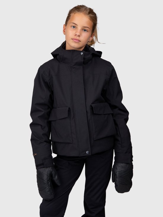 Een jong meisje met blond haar draagt een zwarte ski-jas van Brunotti met vier zakken op de voorkant. Ze draagt ook zwarte handschoenen.