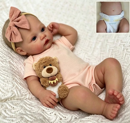 Levensechte babypop met roze strik op haar hoofd, roze rompertje en een knuffelbeer in haar armen.