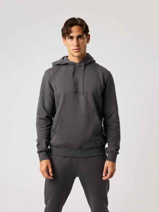 Man in donkergrijs joggingpak, hoodie met capuchon en steekzak. Een label met 'Björn Borg' is zichtbaar.