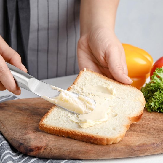 Handen verspreiden boter op een snee brood met een zilverkleurig botermes.