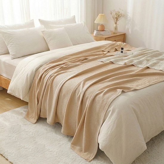 Een beige deken met een subtiel ruitpatroon ligt op een opgemaakt bed met witte lakens.