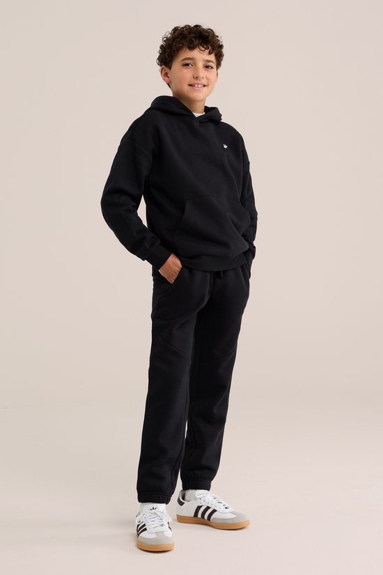 Jongen in een zwarte joggingbroek en hoodie met klein geborduurd logo op de borst.