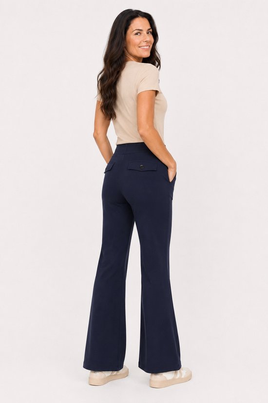 Vrouw in een beige top en marineblauwe flared broek met twee achterzakken, van achteren gezien.