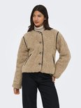 Model draagt een bruine teddy jas met zwarte biezen en knopen, gecombineerd met een coltrui en jeans.