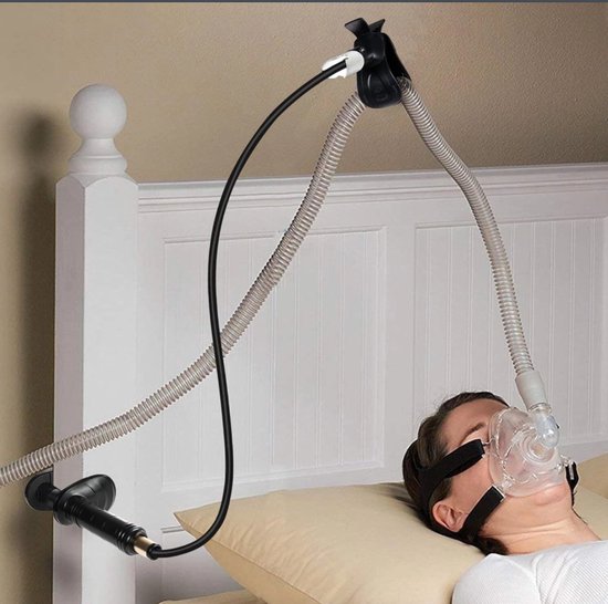 Vrouw slaapt met CPAP-masker en slang, die omhoog wordt geleid door een zwarte, gebogen houder.