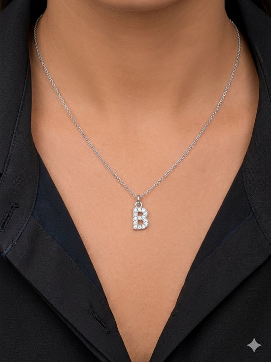 Collier argenté avec pendentif lettre B orné de strass, porté sur une chemise noire.