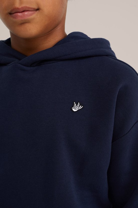 Detail van een donkerblauwe hoodie met kleine witte vogelembroidery op de borst. Jongen draagt de hoodie.