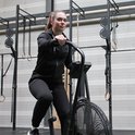 Vrouw met paardenstaart in een zwarte hoodie en zwarte broek, op een hometrainer.