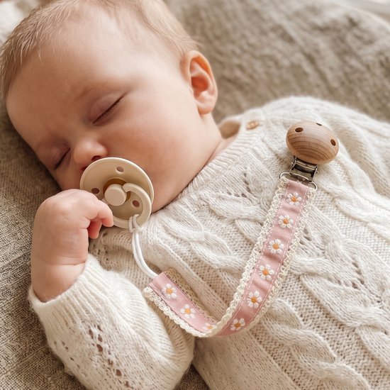 Slapende baby met speen en roze speenkoord met witte madeliefjes en houten clip, gedragen op een gebreide trui.