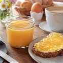 Glazen pot met lichte honing, naast een boterham met jam, ontbijt en koffie.