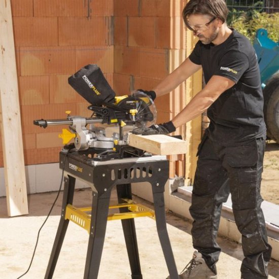 Man gebruikt een gele en zwarte afkortzaag op een werktafel om een houten balk door te zagen.