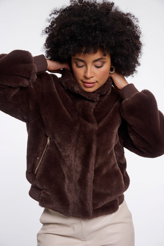 Een model draagt een bruine Faux Fur bomberjack met hoge kraag en leren sluitingen. Ze draagt een lichte broek.