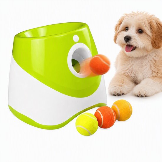 Automatische ballenwerper in wit en groen met drie ballen: geel, oranje en geel. Een hond kijkt toe.