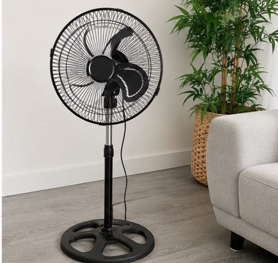 Ventilateur sur pied noir à 3 pales sur une base ronde, à côté d'un canapé et d'une plante.