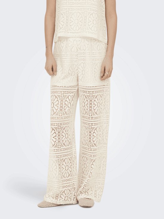 Vooraanzicht van een model in een crèmewitte kanten broek met wijde pijpen en een bijpassende top.