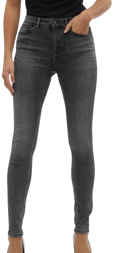Model in strakke grijze jeans met hoge taille, met de hand in de zak.