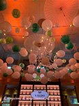 Een interieur met veel witte en groene lampionnen, parasols en een kroonluchter aan het plafond. Oranje gloed.
