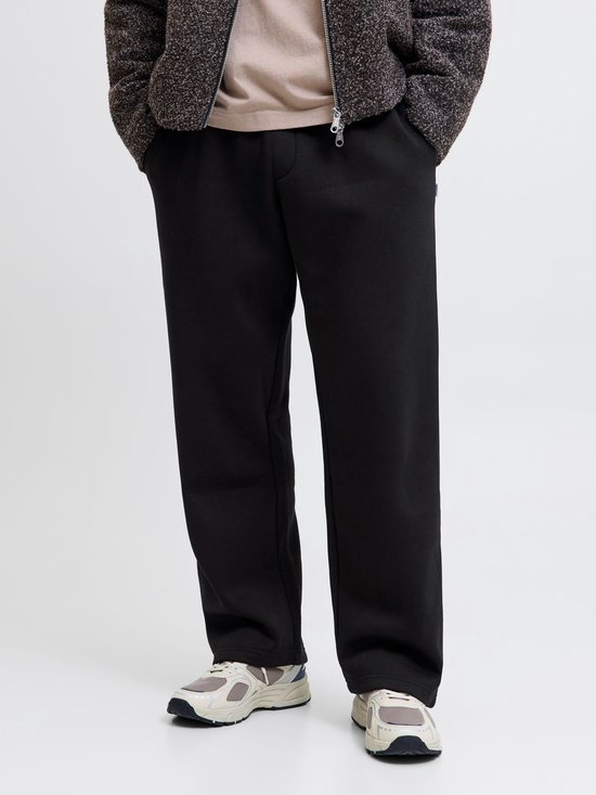 Model draagt zwarte wide-leg joggingbroek, beige t-shirt, getextureerde jas en sneakers.