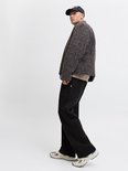 Zijaanzicht: model in zwarte wide-leg joggingbroek, beige t-shirt, getextureerde jas en pet.