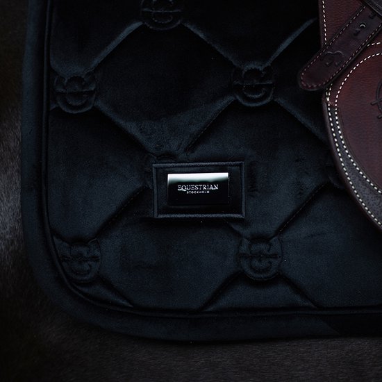 Detail van een zwart zadeldek met Equestrian Stockholm metalen label en monogram stiksels.