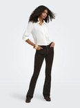 Model met krullend haar draagt een bruine corduroy flared broek en witte blouse.