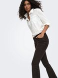 Model met krullend haar draagt een bruine corduroy flared broek en witte blouse, handen in de zakken.
