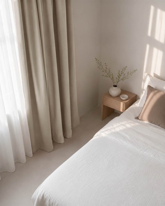 Lichtbeige verduisterende gordijnen met plooiband en witte voile hangen naast een bed in een slaapkamer.