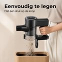 Vrouw in beige trui en witte broek leegt de zwarte steelstofzuiger in een prullenbak met één druk op de knop. "Eenvoudig te legen Met één druk op de knop".