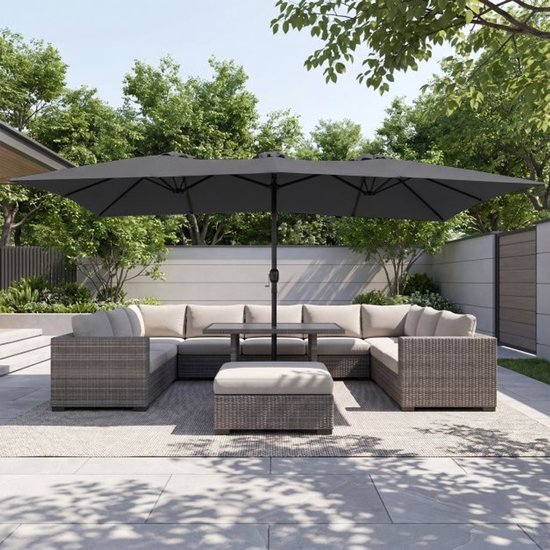 Een grote, dubbele grijze parasol met een opengewerkt dak boven een modulaire, grijze rotan loungeset met beige kussens.