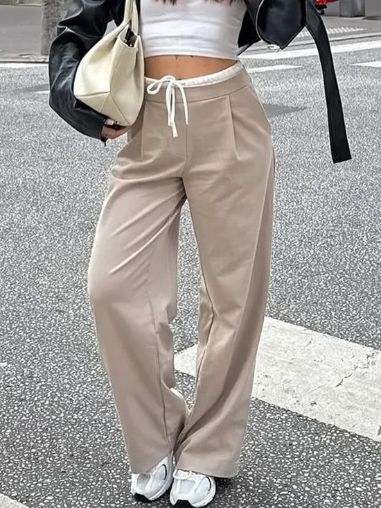 Model in beige wijde broek met trekkoord, witte crop top en sneakers