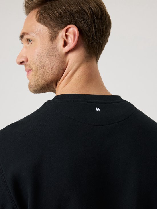 Achterkant van een zwarte sweater met een wit logo in de nek.