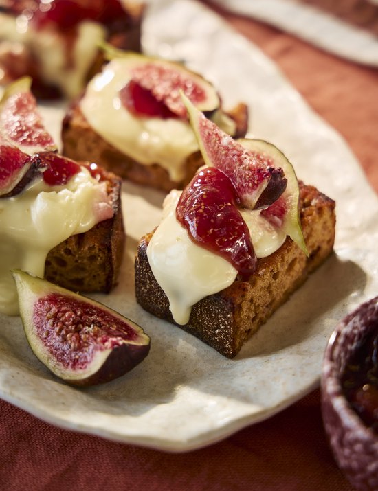 Gebakken sneetjes brood belegd met gesmolten kaas, verse vijgenplakjes en een rode vruchtengelei.
