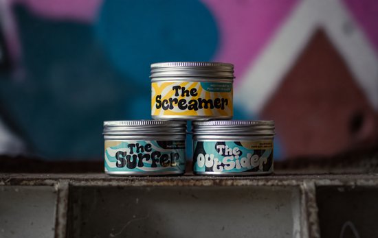 Drie zilveren blikjes met labels: 'The Screamer' bovenop, 'The Surfer' links en 'The Outsider' rechts. Gebruikt in een industriële omgeving.