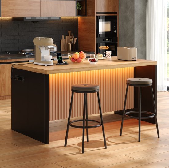 Îlot de cuisine avec plan de travail en bois, côtés noirs, rainures, éclairage et deux tabourets. Une cafetière, un grille-pain et des fruits sont sur l'îlot.