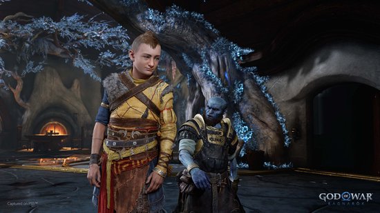 Atreus, gekleed in een geel-bruine tuniek, staat naast een blauwe Fom de speler in de game God of War: Ragnarök.
