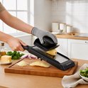 Hand snijdt aardappel met zwarte mandoline snijder op houten snijplank. Geraspte kaas, uien, olijfolie en salade.