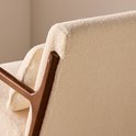 Detail van de achterkant van een schommelstoel met crèmekleurige bouclé bekleding en een walnootkleurig houten frame.
