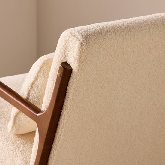 Detail van de achterkant van een schommelstoel met crèmekleurige bouclé bekleding en een walnootkleurig houten frame.