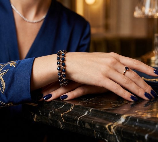 Model met donkerblauwe nagels draagt een gouden armband met blauwe kralen en een bijpassende ring.