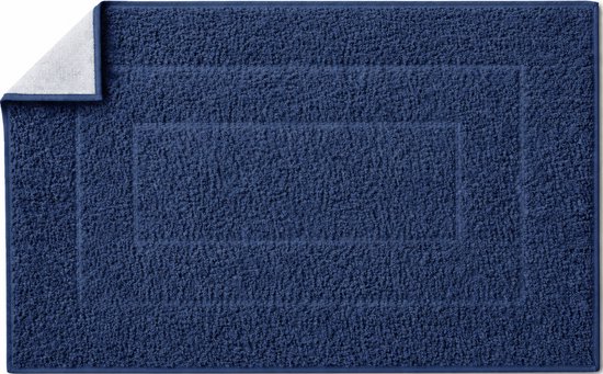 Donkerblauwe badmat met een zachte, ribbelige textuur. Hoek opgelicht met witte badstof.