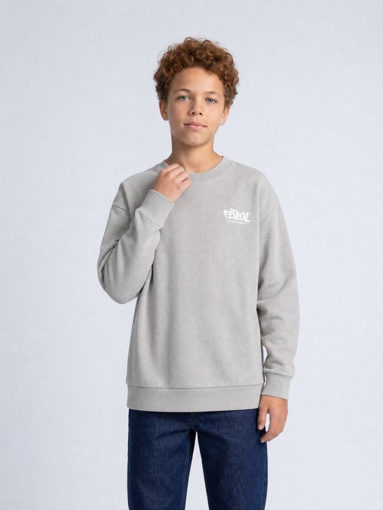 Jongen met grijze sweater met witte 'Petrol' logo op de borst, blauwe jeans.