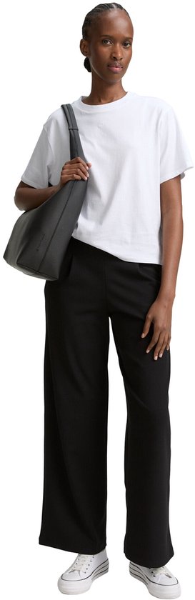 Model draagt een zwarte wijde broek met witte sneakers en een witte T-shirt.