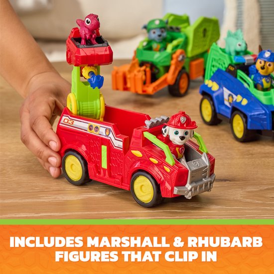 Een rode Paw Patrol dino rescue brandweerwagen met Marshall en dinosaurusfiguur, in de handen van een kind. Op de achtergrond andere Paw Patrol voertuigen.