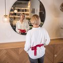 Vrouw in wit shirt knoopt een rood warmtekussen om haar middel, kijkt in spiegel.