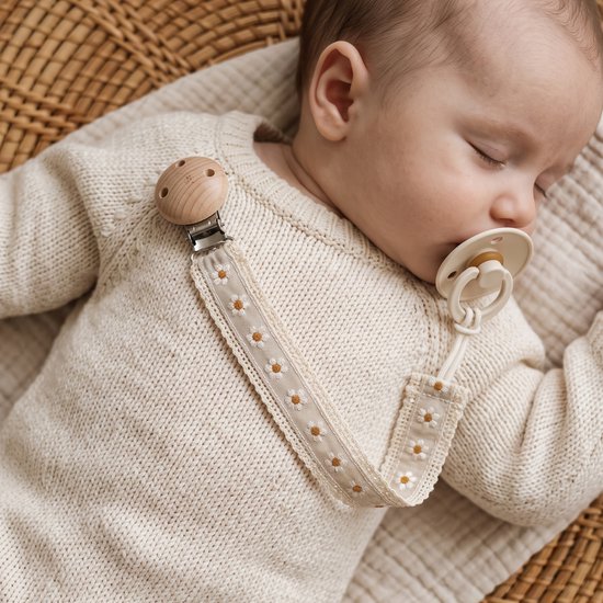 Baby in beige gebreide trui, slapend met grijze fopspeenhouder met madeliefjes en houten clip.