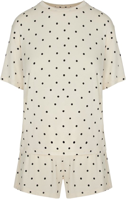Crèmekleurige pyjamaset met zwarte polkadotprint. T-shirt met korte mouwen en korte broek, op witte achtergrond.