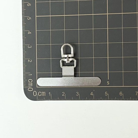 Zilverkleurige telefoonkoordclip op een snijmat, gemarkeerd met centimeters.