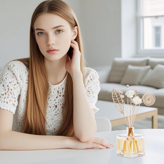 Vrouw met lange blonde haren en witte kleding, bij een tafel met een diffuser met natuurlijke geurstokjes.